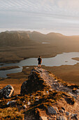 Wanderer auf einem Bergfelsen genießt den Blick auf den Sonnenuntergang, Assynt, Sutherland, Schottland