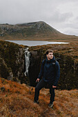Man hiking along remote mountain waterfall, Assynt, Sutherland, Scotland\n
