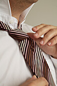 Extreme close up of man's hands tying a neck tie\n