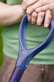 Extreme close up of hands on garden tool handle\n