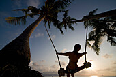 Young woman at sunset on a swing between palm trees, Thailand\n