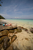 Young woman lying on rocks sunbathing and relaxing, Koh Phi Phi, Thailand\n