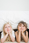 Zwei junge Mädchen mit auf Händen ruhendem Kinn unter dem Bett