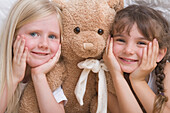 Close up of two young girls with teddy bear smiling\n