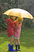 Zwei junge Mädchen im Regen unter gelbem Regenschirm