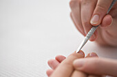 Close up of manicurist's hand pushing woman's cuticles with cuticle pusher\n