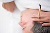 Close up of man's head with burning ear candle\n