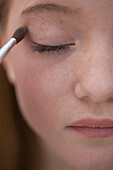 Close up of young woman applying eye make-up with eyeshadow brush\n