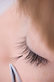 Close up of young woman applying individual eyelash with tweezers\n