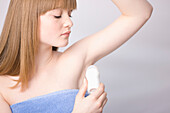 Close up of young woman applying deodorant under armpits\n