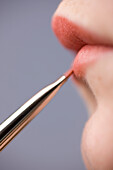 Close up of young woman lips with lipstick brush\n