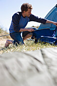 Porträt eines jungen Mannes, der hockend ein Zelt aufbaut
