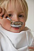 Close up of young blonde boy drinking water with a spoon\n