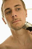 Young man shaving with electric razor\n