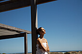 Woman wearing towel leaning against wooden beam relaxing\n