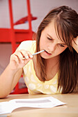 Young girl studying with pencil in mouth\n