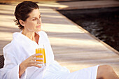 Woman sitting and drinking apple orange juice by swimming pool\n