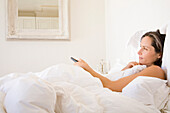 Woman lying in bed changing channel with remote control\n