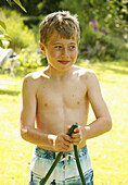 Young boy standing holding garden hose\n