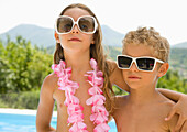 Young boy and young girl wearing oversized sunglasses\n