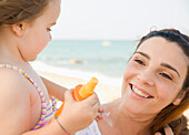 Daughter applying suntan lotion on mother's neck\n