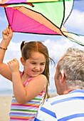 Young girl holding kite and smiling to her father\n