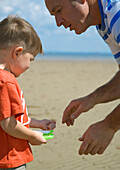 Father talking to young boy holding kite flying line\n