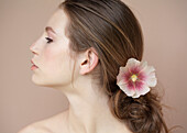 Profile of beautiful young woman with flower holding hair back\n