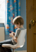 Porträt eines Jungen, der auf einem Handy sitzt und Textnachrichten schreibt, mit Blick auf die Schlafzimmertür