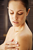 Portrait of a young woman applying body lotion on shoulder\n