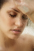 Close up of a young woman leaning against steaming shower door\n