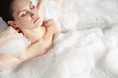 Portrait of a young woman having a bubble bath and relaxing\n