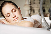 Woman relaxing her head against edge of bathtub\n