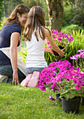 Back of mother and daughter kneeling in the garden tending plants and smiling\n