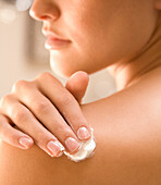 Close up of a young woman hand applying body lotion on shoulder\n