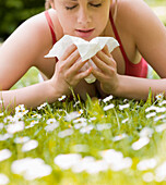 Young woman lying on stomach on the grass sneezing\n