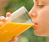 Nahaufnahme einer jungen Frau, die ein Glas Orangensaft trinkt und hält - Profil