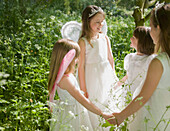 Young girls in fancy dress holding hands in a garden\n