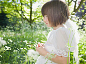 Portrait of young girl in a white fairy costume standing in a garden\n