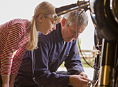 Young girl helping grandfather repairing motorbike\n