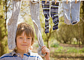 Close up of young boy standing between socks hanging from clothes line\n