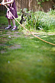 Headless young girl pulling garden hose\n