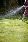 Headless young girl spraying the lawn with garden hose\n