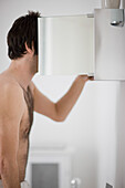 Shirtless young man looking inside a bathroom cabinet\n