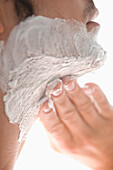 Close up of a young man applying shaving cream on his neck\n