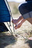Ein Camper befestigt mit den Händen die Zeltstange