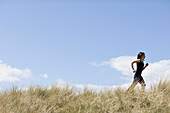 Young woman running through sand dunes\n