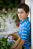 Young boy holding a brown paper bag full of fruit and vegetables\n