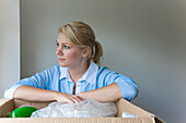 Close up of a young woman with arms resting on a cardboard box looking out\n