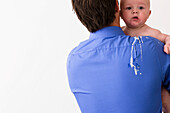 Back view of a man holding a baby with vomit on his back and shoulder\n